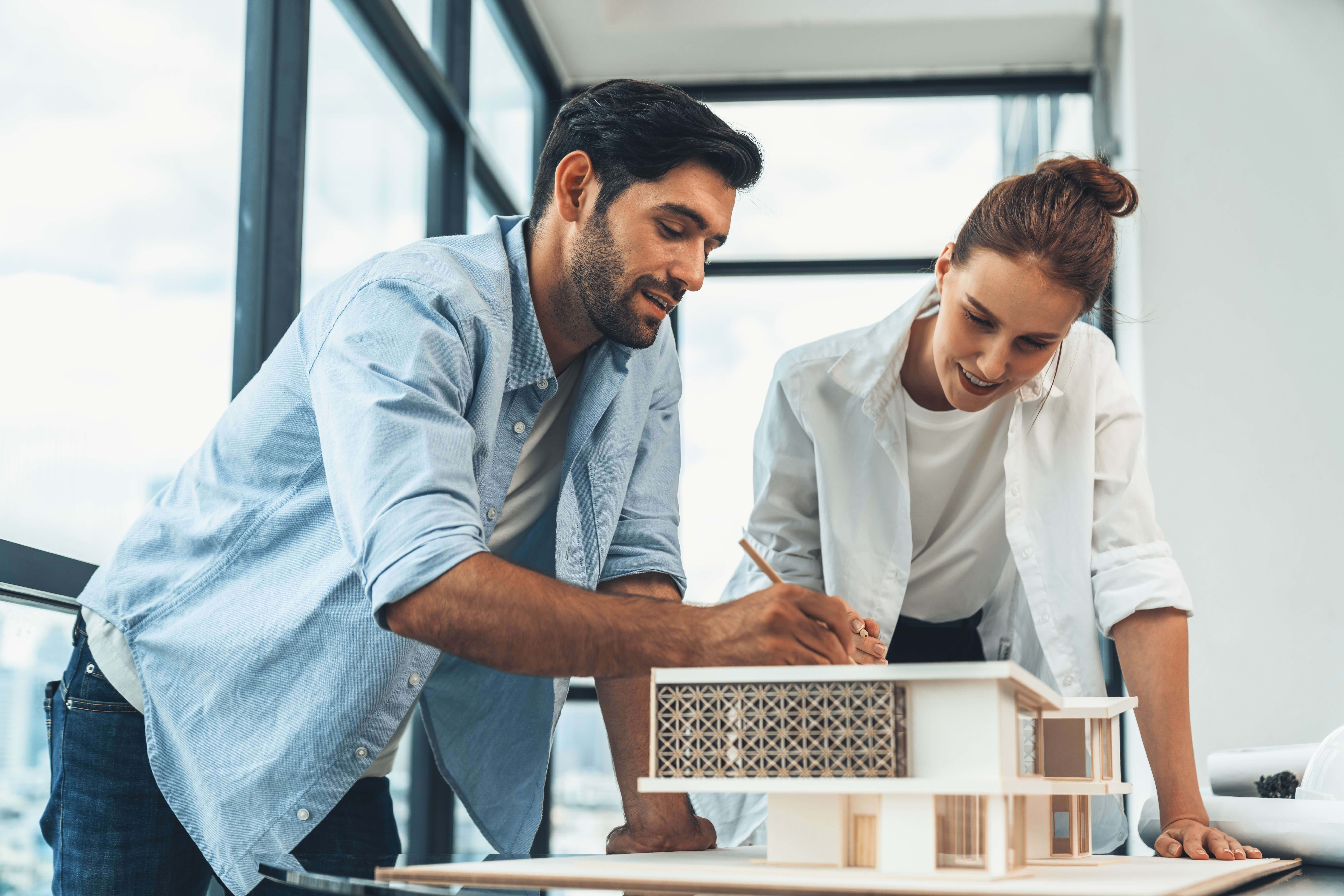 Two architects working on a scale model of a modern house in a bright office.